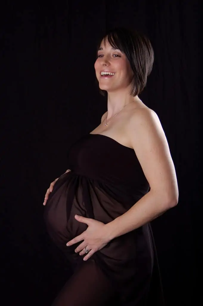 maternity photography in baltimore of a mother wearing all black sheer dress on a black background