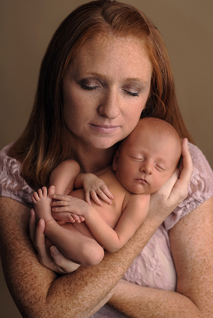 Picture of a mother holding her newborn baby girl in her arms by baltimore newborn photographer Angela Singleton