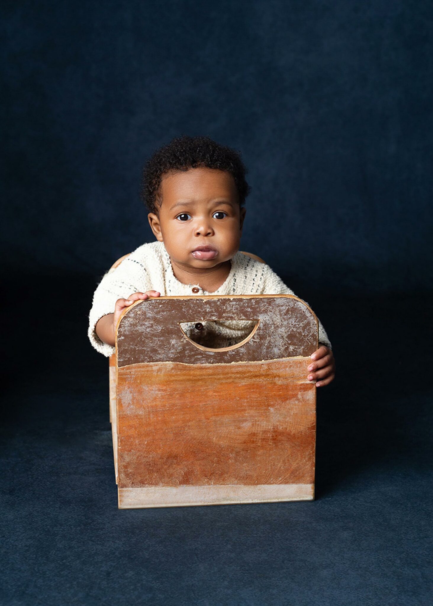 sitter session of little boy sitting in a baby wooden bed with bright eyes 
