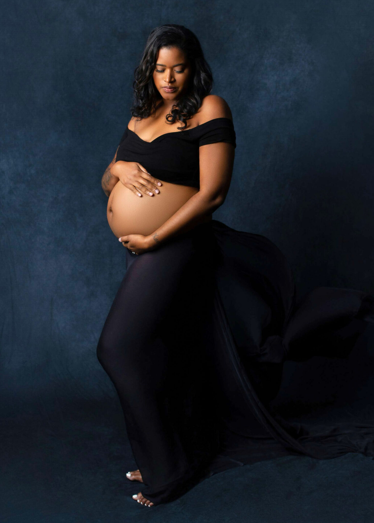 baltimore pregnancy photo on an expecting mother wearing a cropped black top and a sheer wrapped bottom show off her belly