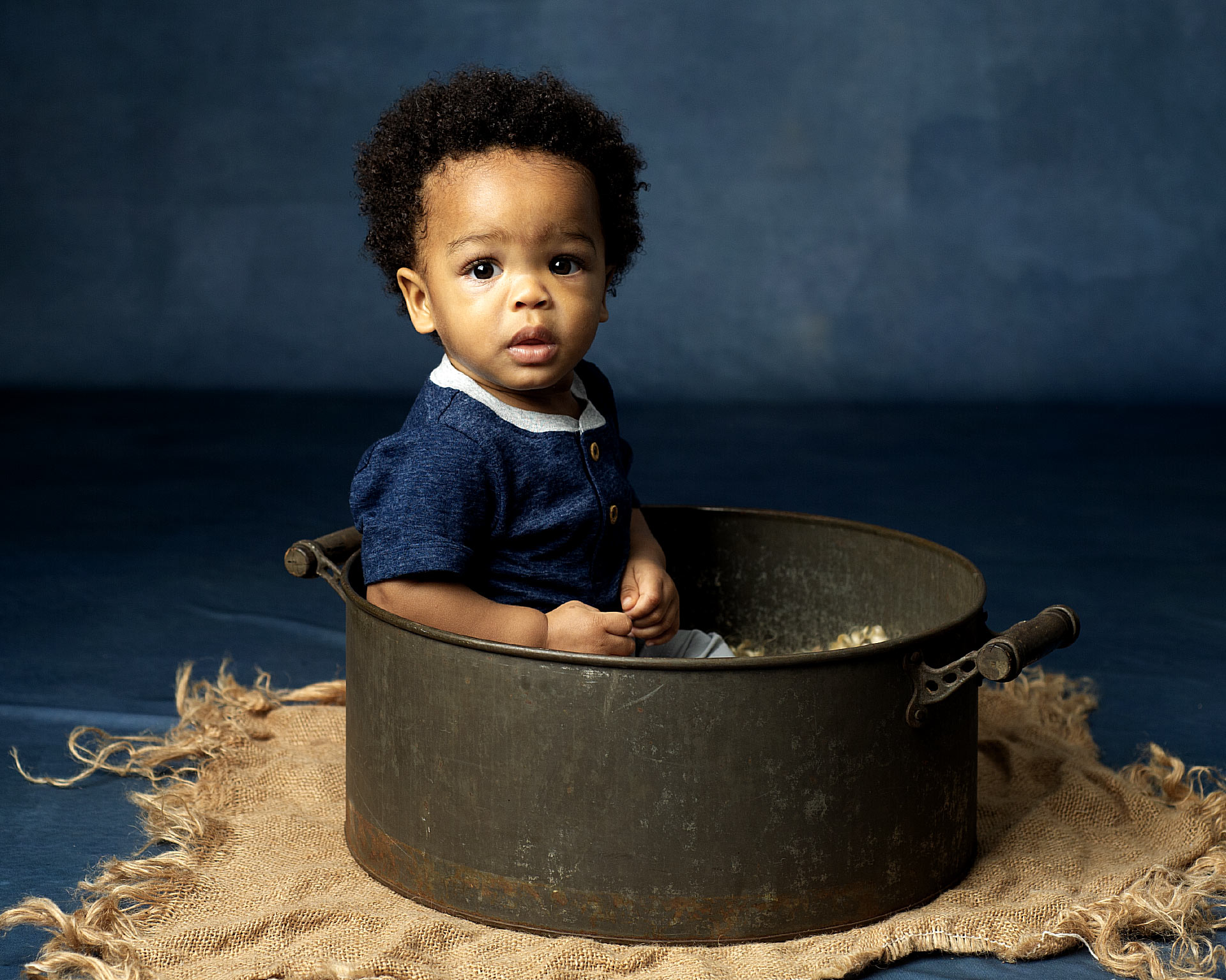 milestone session of little boy sitting in a pot on a blue background 