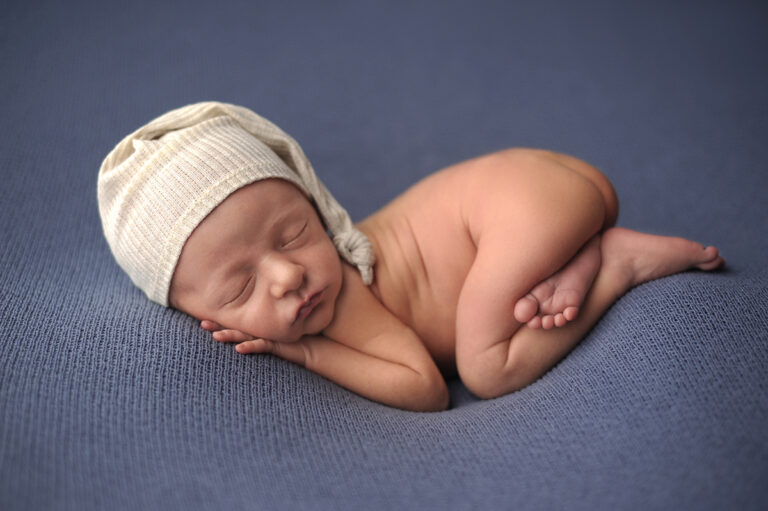 picture of boy wearing a sleepy hat laying on blue curled up
